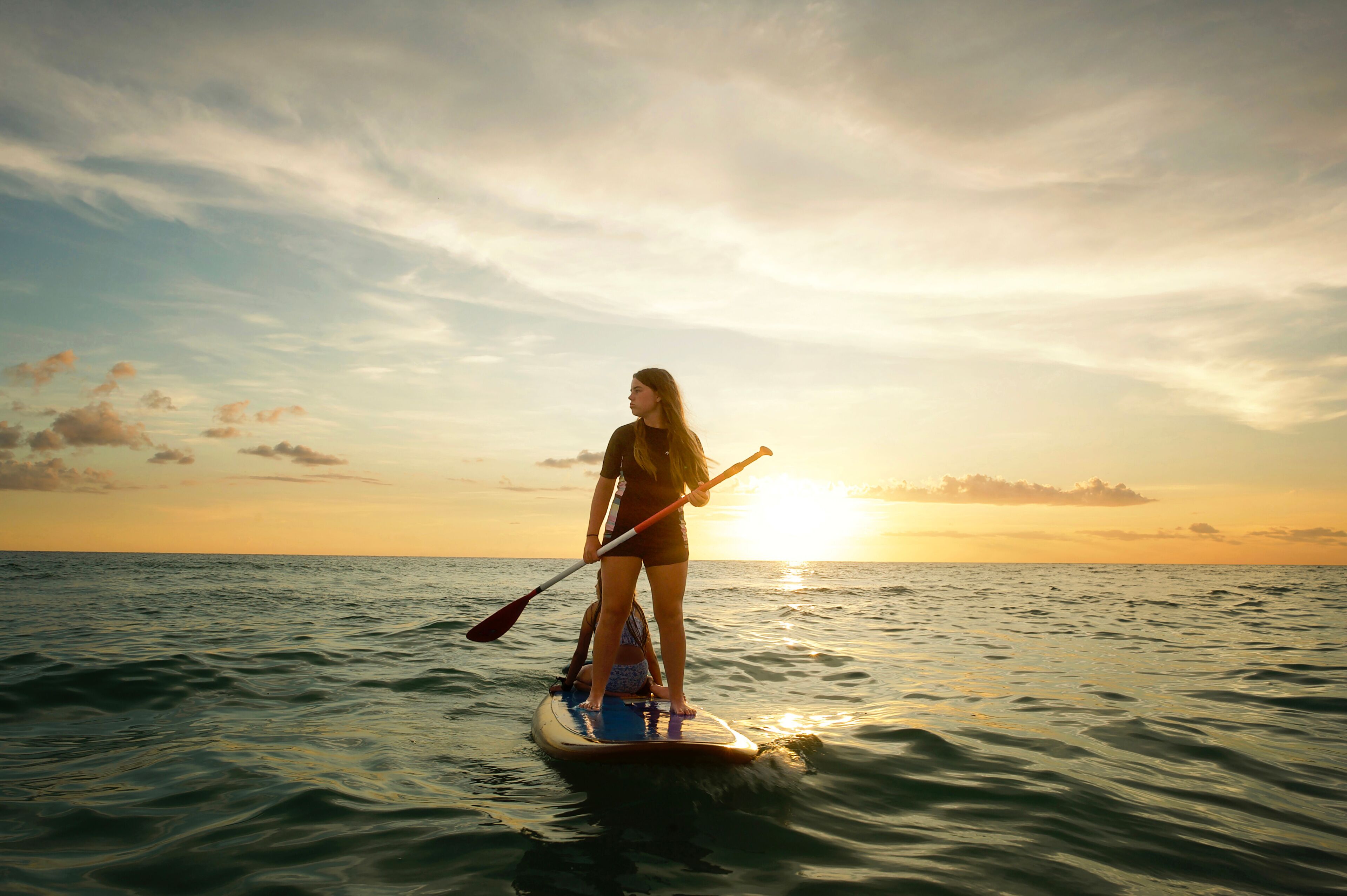 A person paddleboarding on calm ocean waters during sunset.