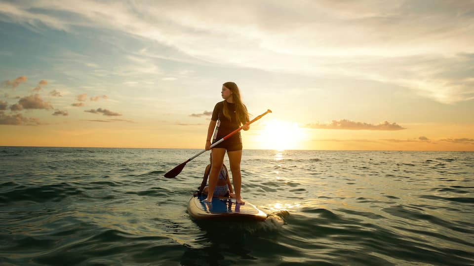 A person paddleboarding on calm ocean waters during sunset.