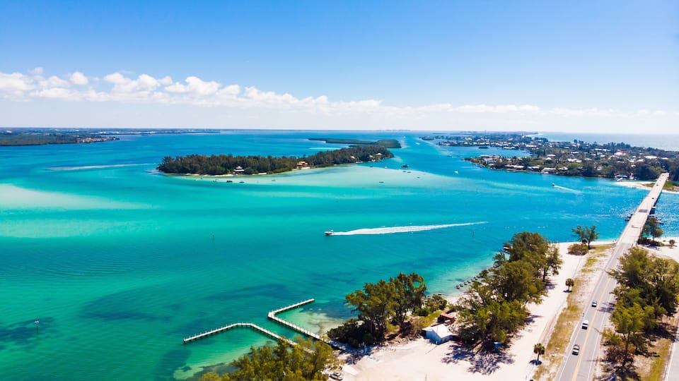 A coastal area with turquoise waters, a pier, a beach, and a road.