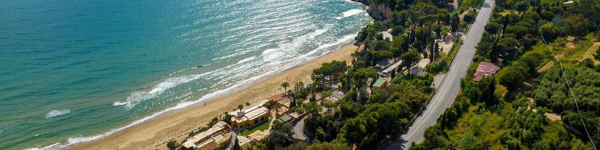 A coastal landscape with a beach, a road, and a hill with vegetation.