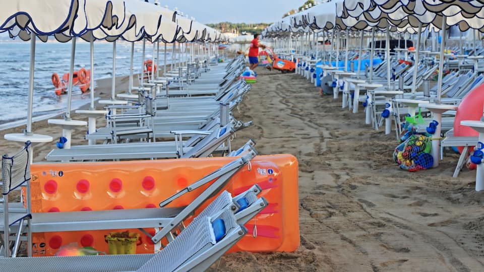 A beach with rows of sunbeds and umbrellas, a lifeguard tower, and a sandy shoreline.