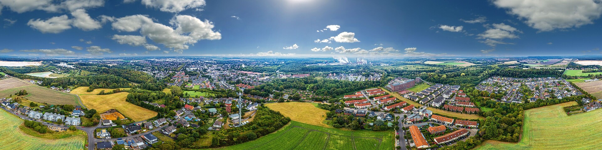 An aerial view of a town with fields, houses, and a large body of water in the distance.