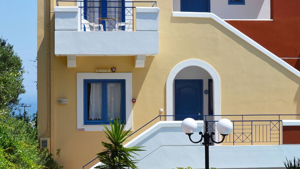 A multi-story building with blue doors and windows, surrounded by potted plants and a tiled walkway.