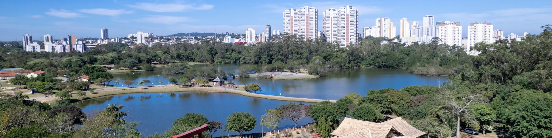 Ein Park mit einem See, einem roten Torii-Tor und einer Skyline mit Hochhäusern im Hintergrund.