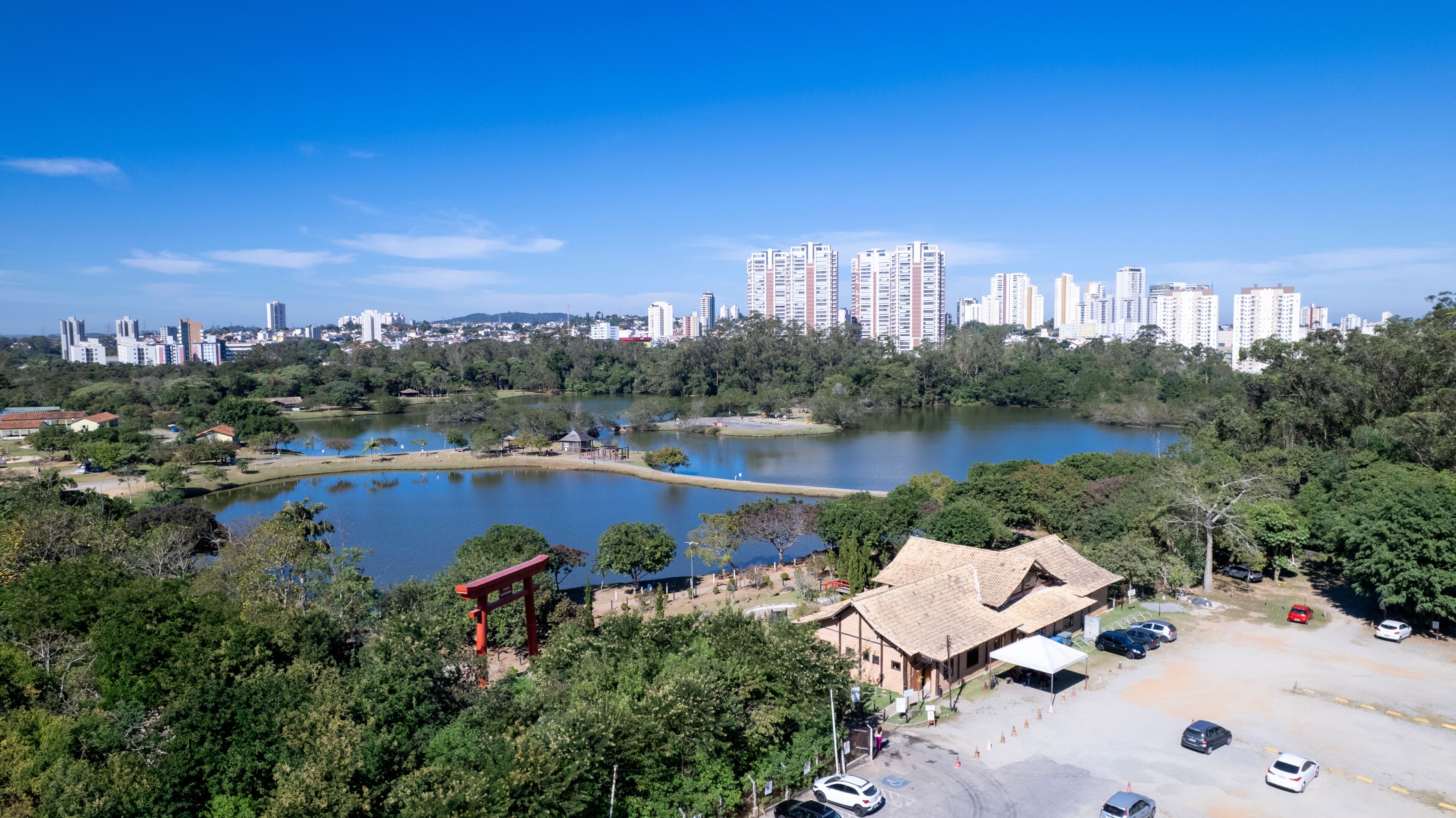 A park with a lake, a red torii gate, and a cityscape with high-rise buildings in the background.