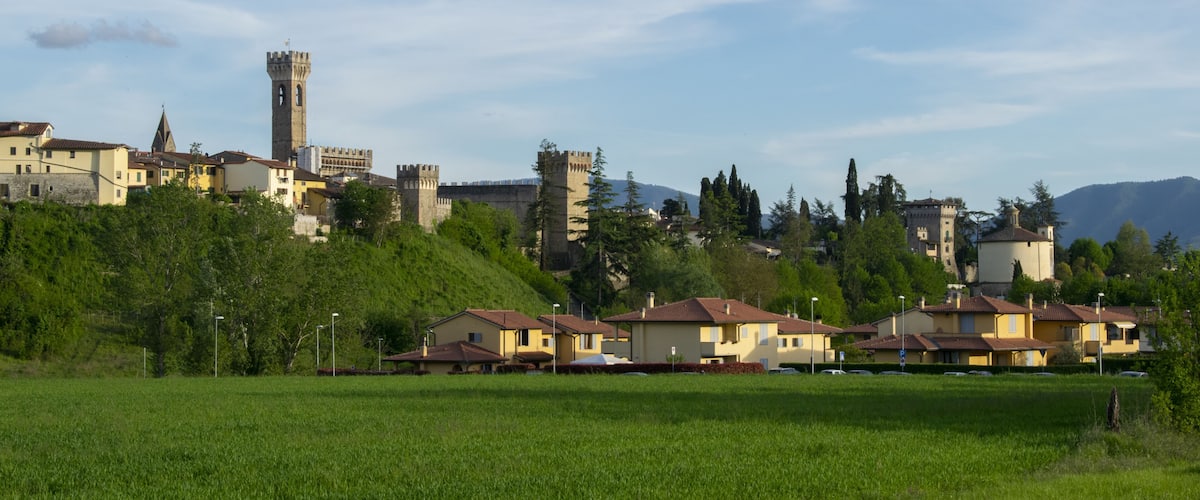 A town with a prominent tower, surrounded by greenery and residential buildings.