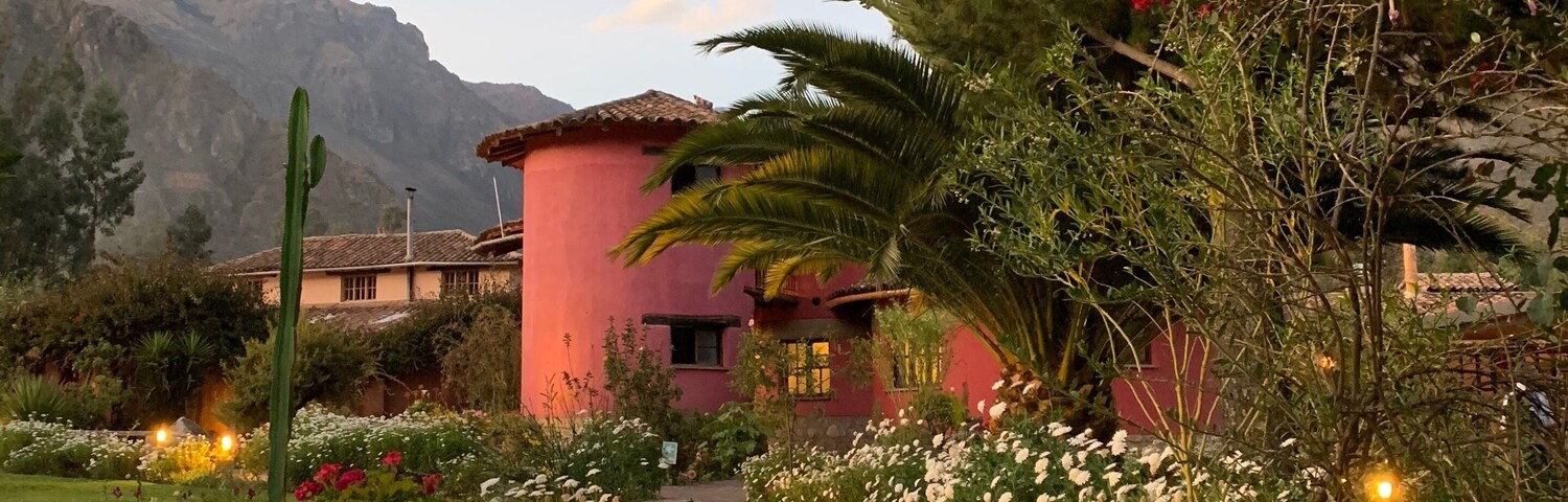 Um caminho de pedra leva a um edifício rosa, rodeado por vegetação exuberante e plantas floridas.