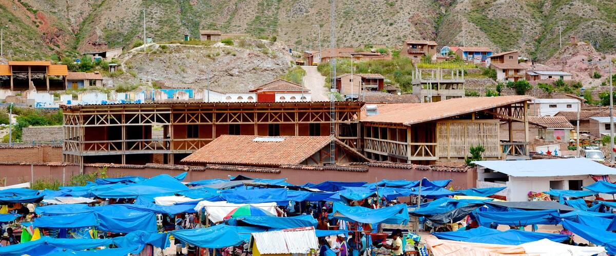 A rural market with blue canopies and a mountainous backdrop.
