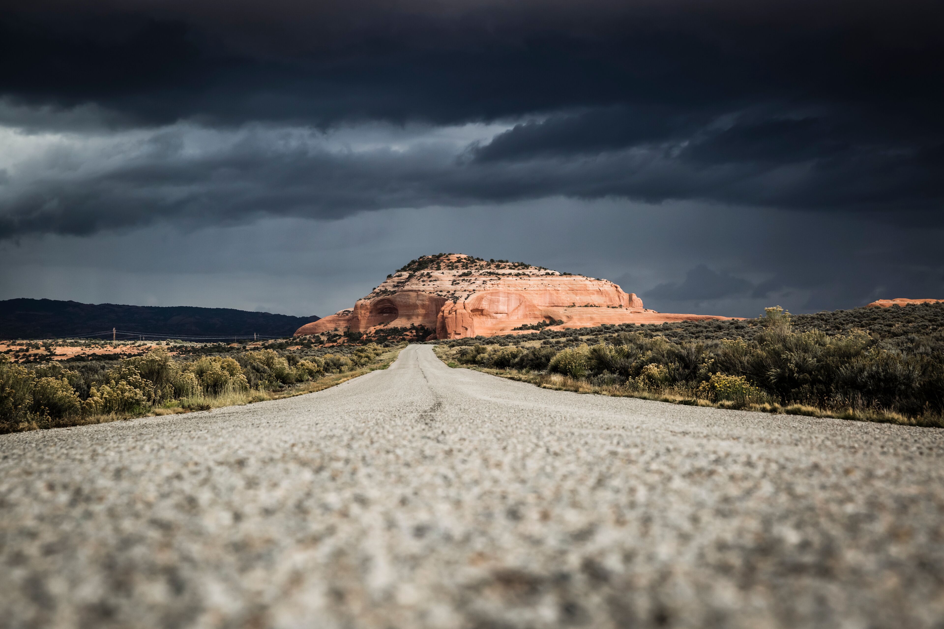 A gravel road leading to a large red rock formation under a stormy sky.