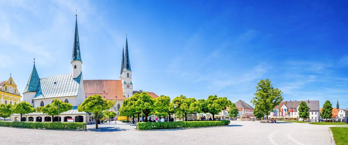 A historic church with two tall spires, surrounded by a cobblestone square and lush green trees.