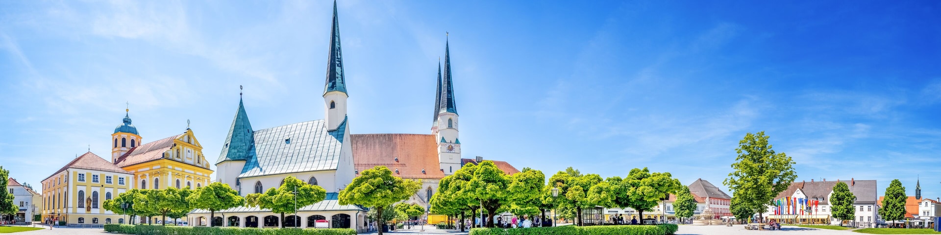 A historic church with two tall spires, surrounded by a cobblestone square and lush green trees.