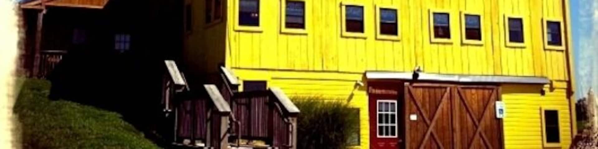 A yellow barn with a red door and windows.