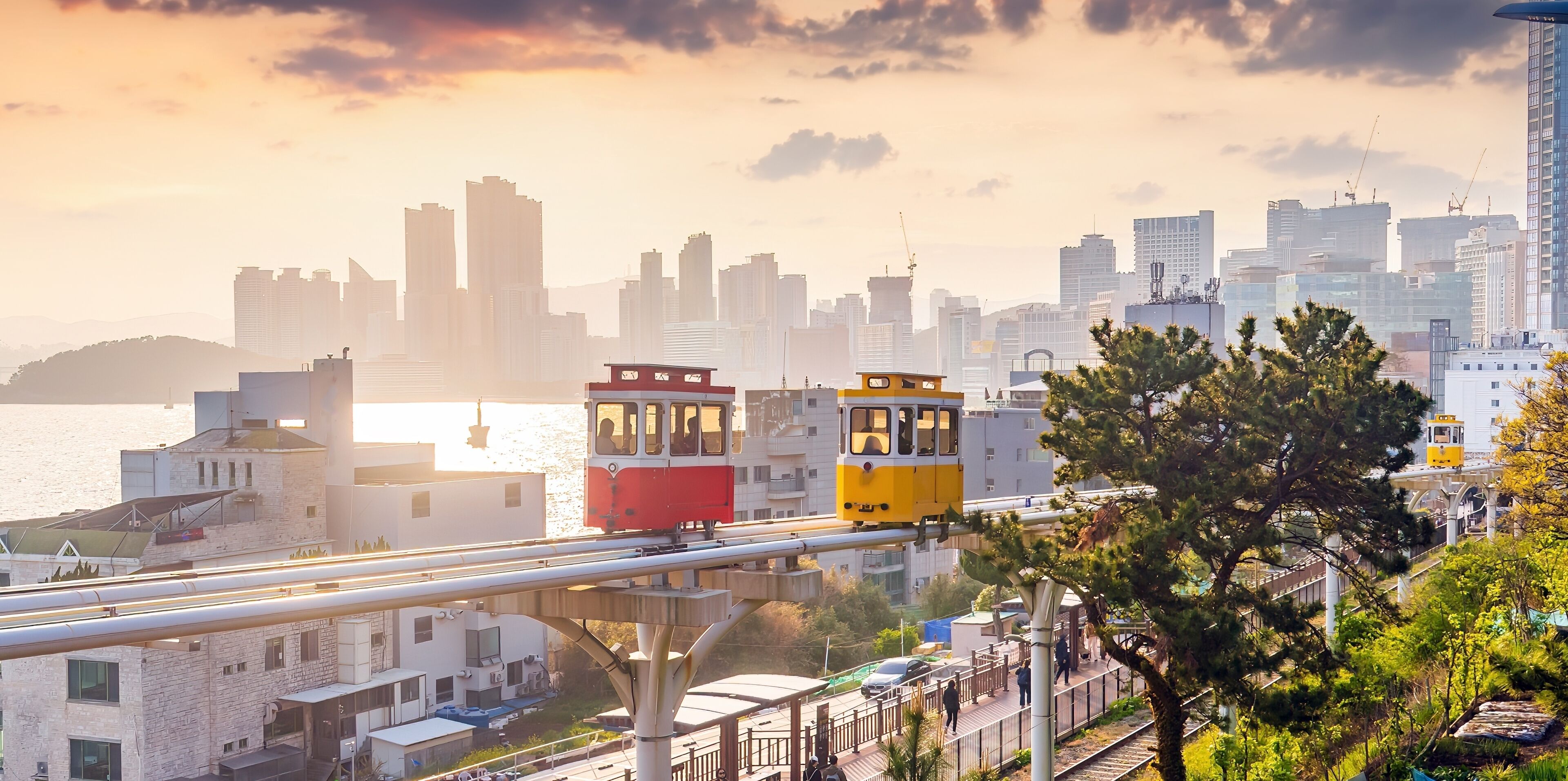 A cityscape with a river, modern buildings, and a tram in the foreground.