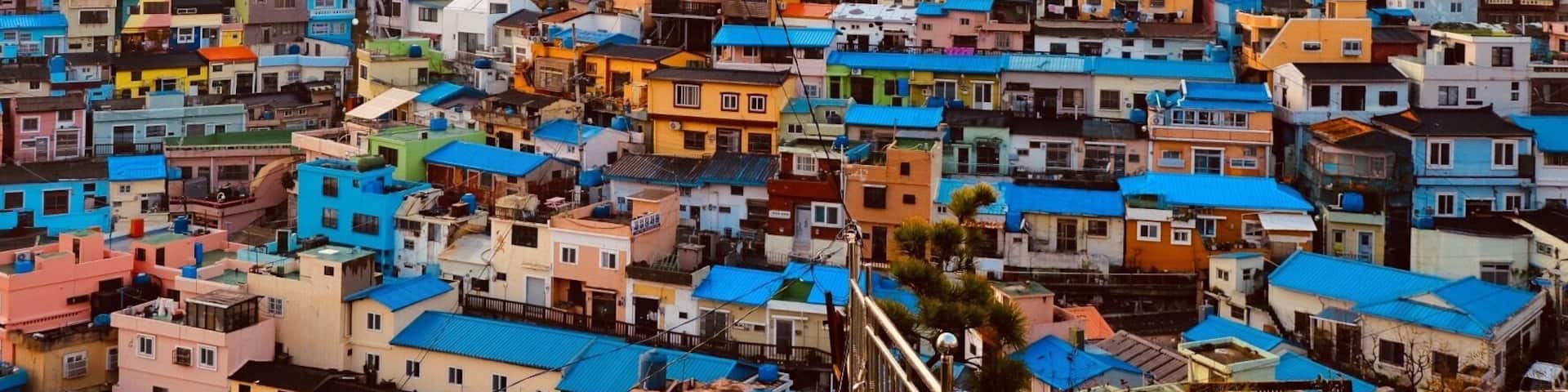 A densely packed hillside settlement with colorful buildings and a forested hill in the background.