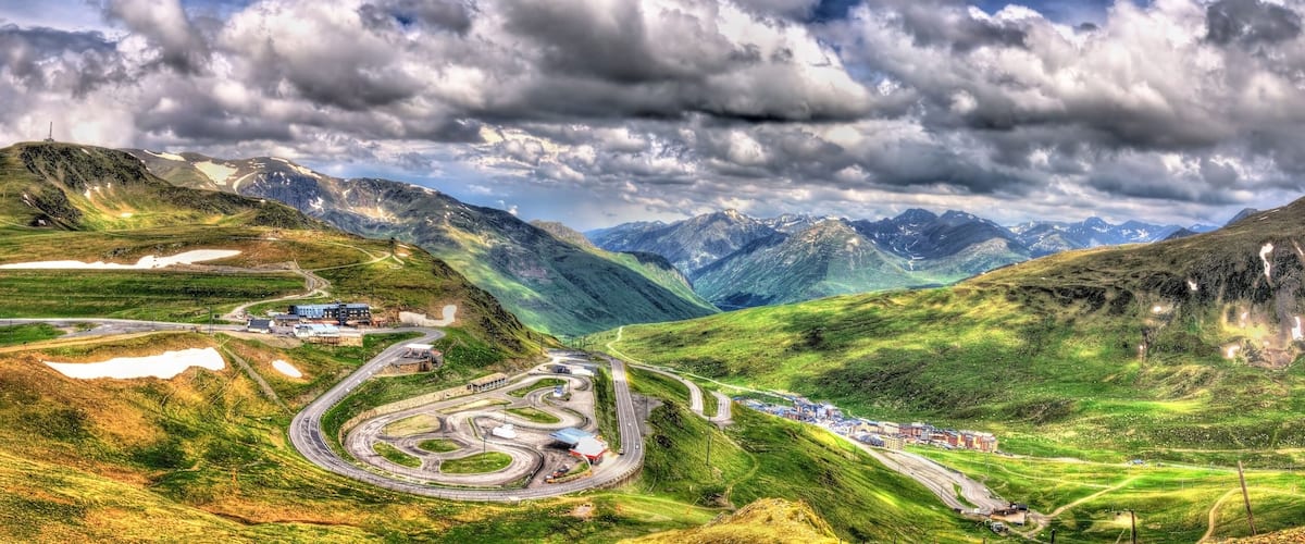 A mountainous landscape with winding roads, a small building, and distant snow-capped peaks.