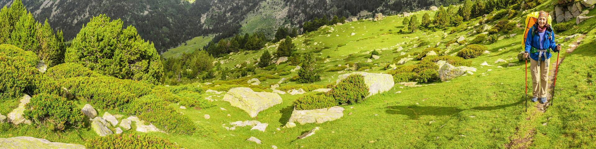 Happy woman hiker travels in Pyrenees Mountains in Andorra and Spain. Nordic walking, recreation and trekking along GR11 path trail