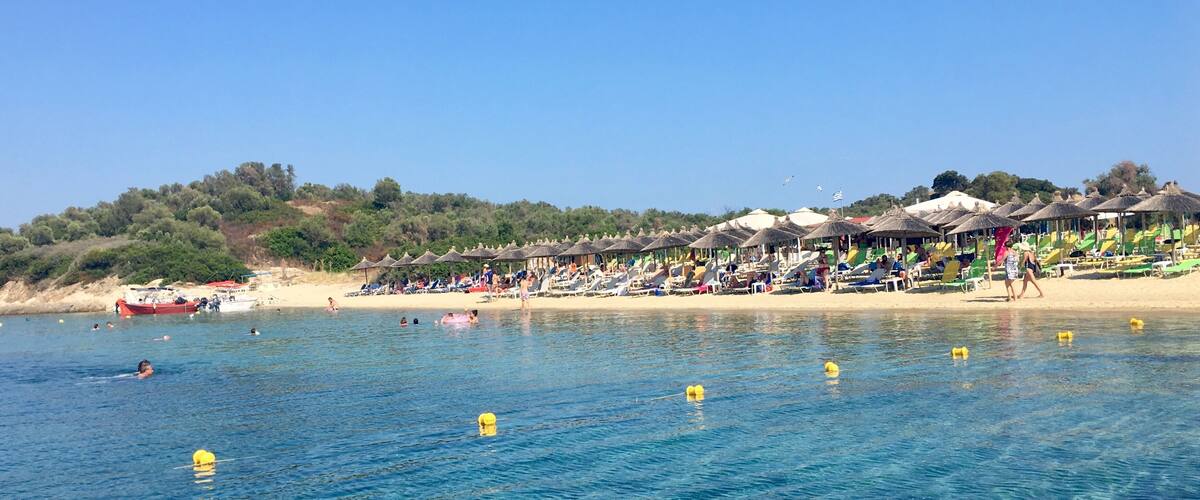 A beach with clear blue water, sun loungers, and umbrellas.