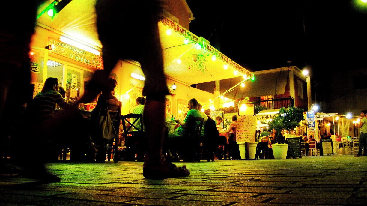 A nighttime outdoor dining area with illuminated signs and tables.