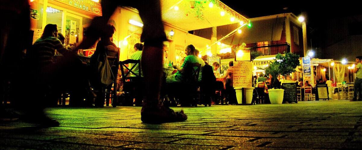 A nighttime outdoor dining area with illuminated signs and tables.