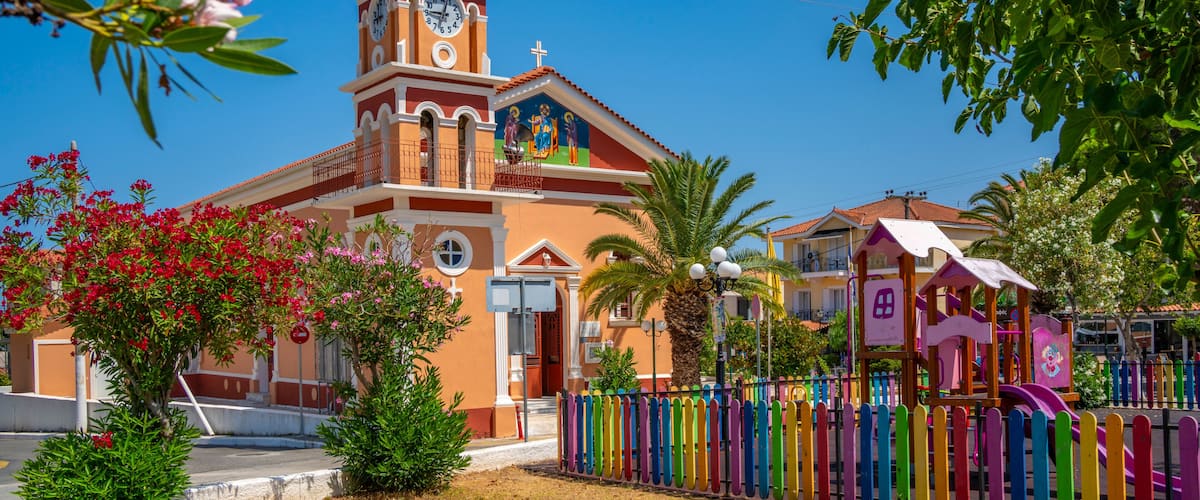 A church with a clock tower, colorful fence, and a playground.