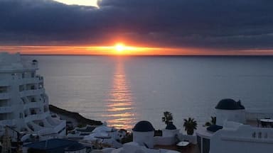 A coastal sunset with white buildings and a calm sea.