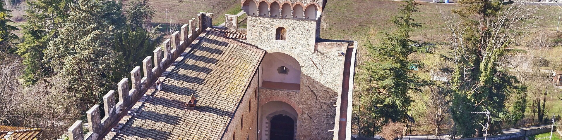 Una torre medieval con tejado de tejas rojas, rodeada de edificios residenciales y campos abiertos.