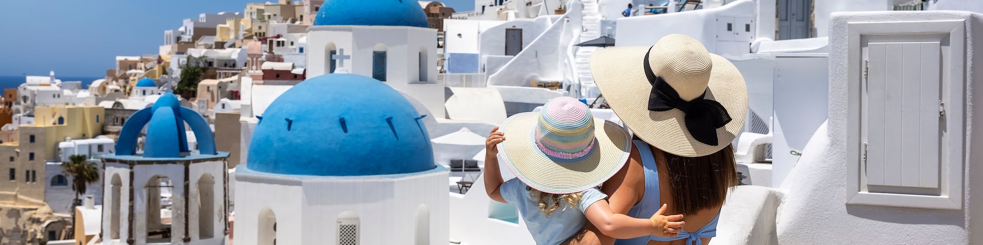 Una mujer y un niño en un edificio blanco con cúpulas azules, con vistas a un pueblo costero.