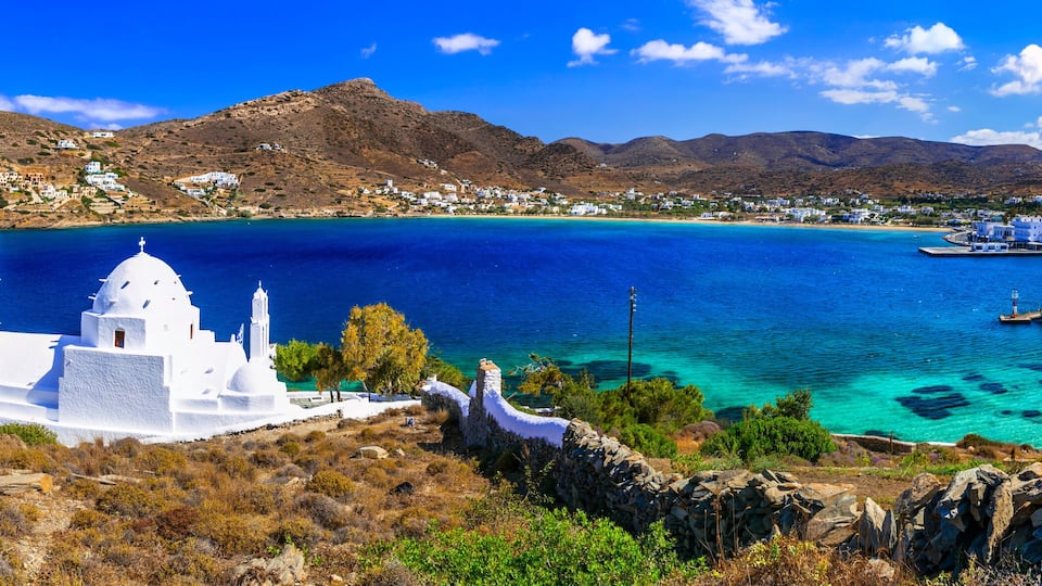 A coastal town with white buildings, a church with a bell tower, and a clear blue sea.