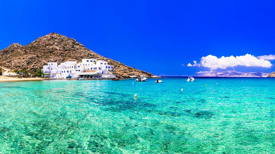 A coastal town with clear turquoise waters, white buildings, and rocky hills.