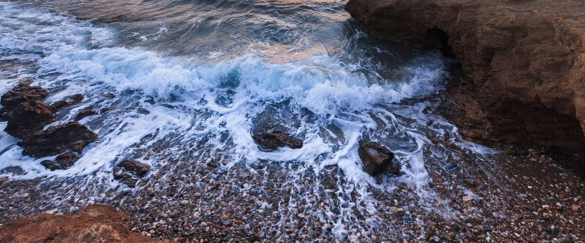 A rocky shoreline with waves crashing against the rocks during sunset.