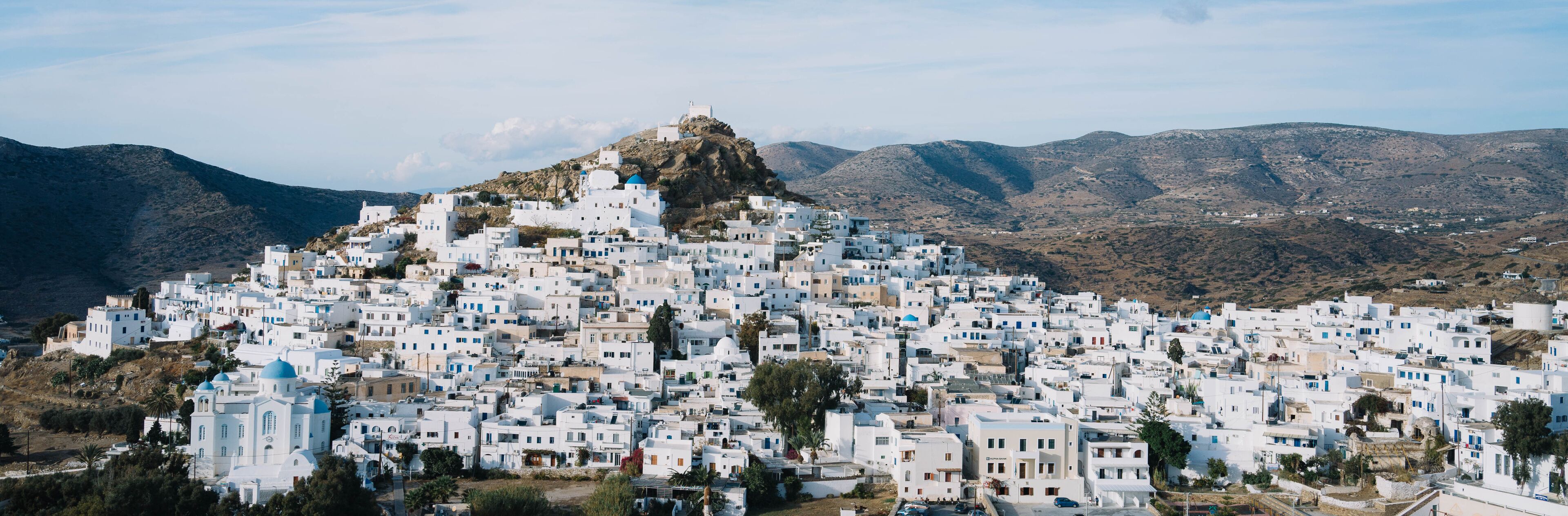 A densely packed white village on a hillside with a prominent church at the top.
