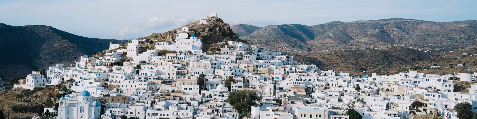 A densely packed white village on a hillside with a prominent church at the top.