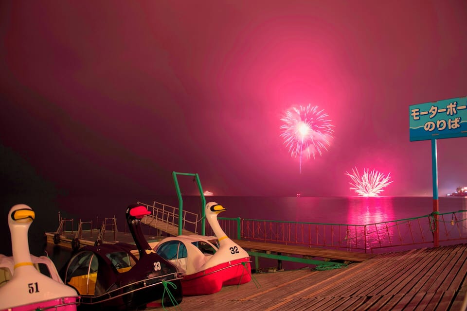 A duck-shaped boat with the number 32 on a dock, fireworks in the background, and a sign with Japanese text.