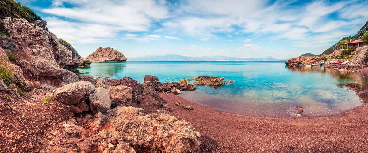 A rocky beach with clear turquoise water, a small island, and a distant mountain range.