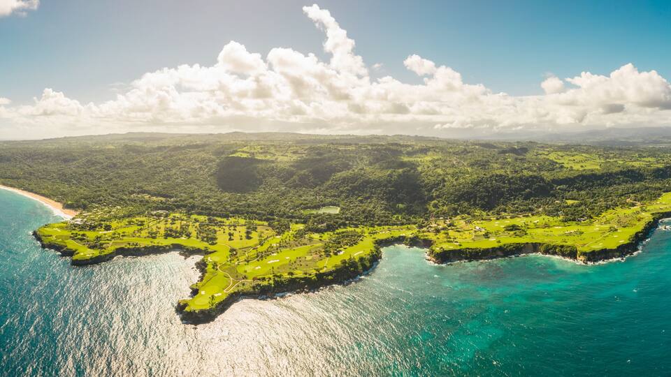 An aerial view of a lush, green island with clear turquoise waters and a sandy beach.