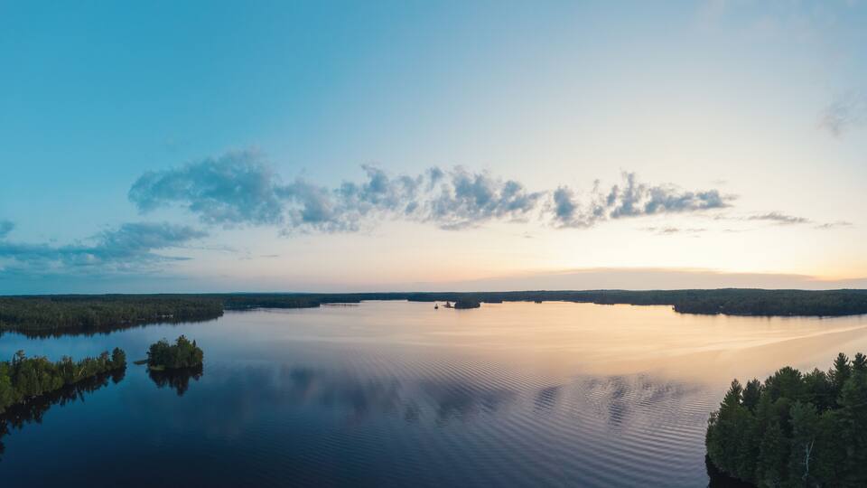 A calm lake surrounded by dense forests under a clear sky.