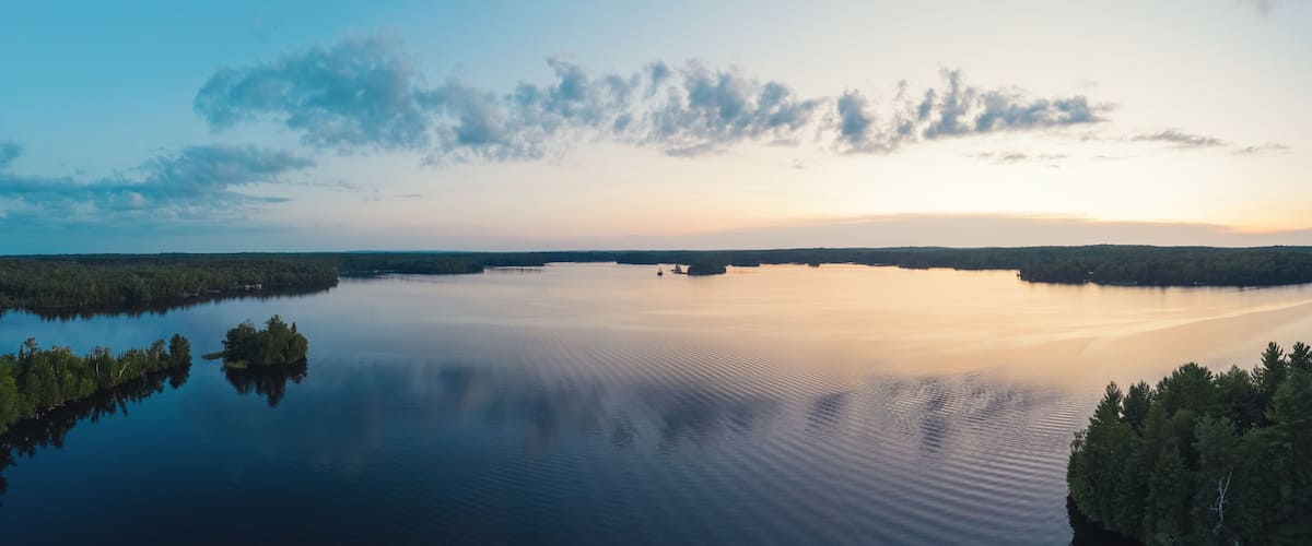 A calm lake surrounded by dense forests under a clear sky.