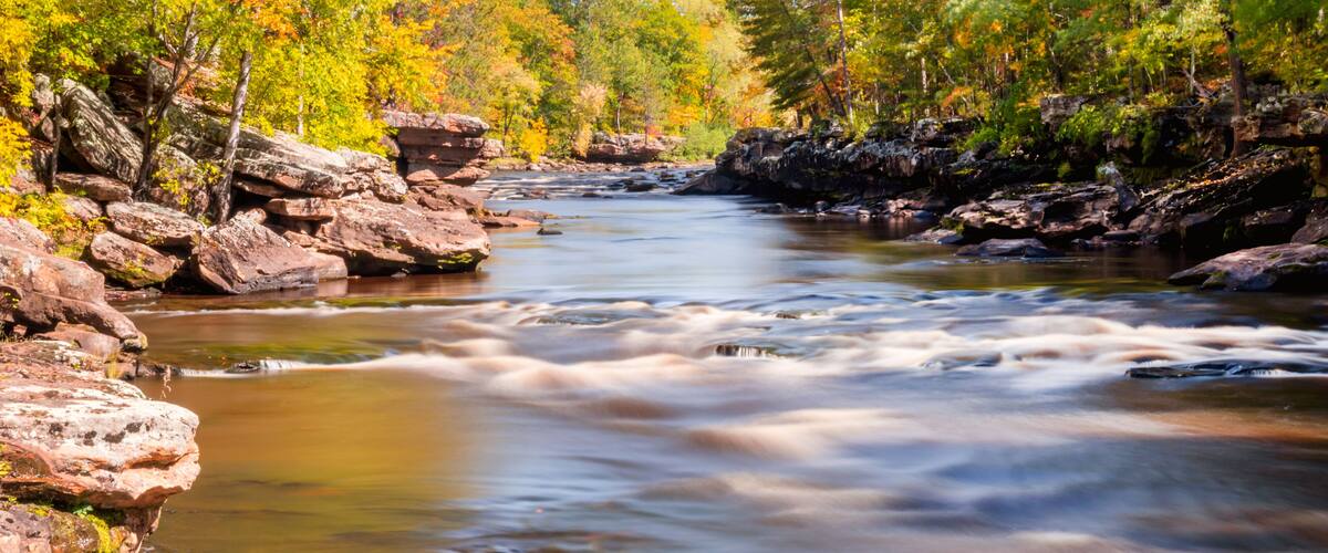 A river flowing through a forest with autumn foliage and rocky banks.