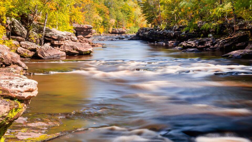 A river flowing through a forest with autumn foliage and rocky banks.