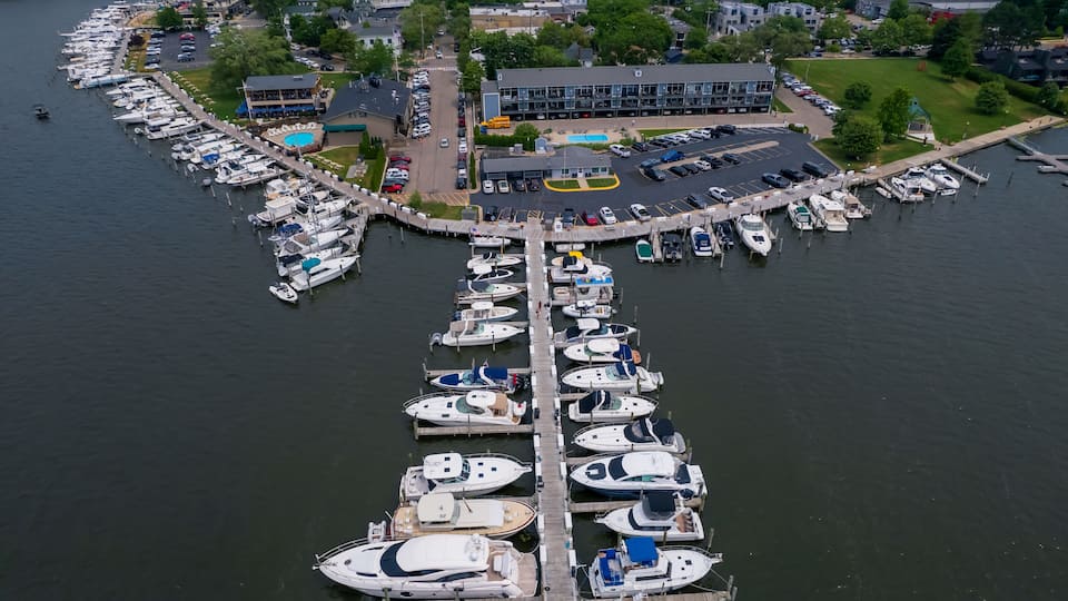 An aerial view of a marina with numerous boats docked at a pier, surrounded by buildings and greenery.
