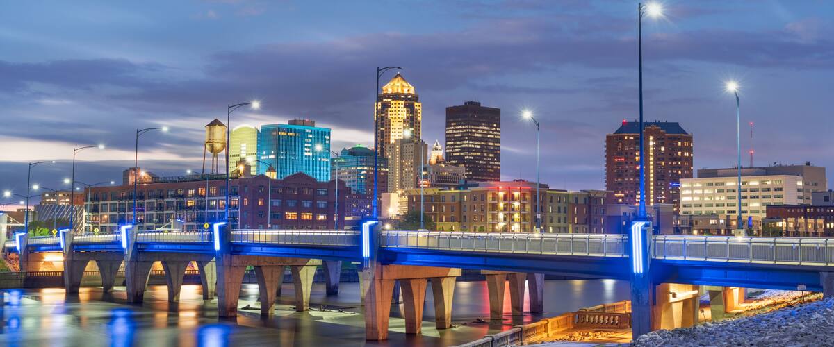 A city skyline at dusk with illuminated buildings, a bridge, and a river.