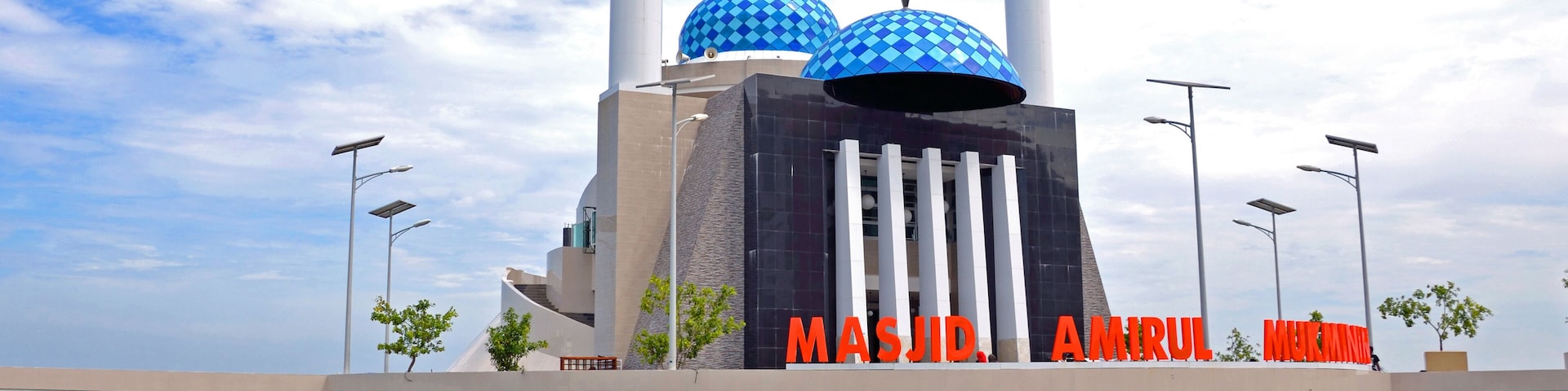 A mosque with blue domes and minarets, located on a waterfront with a clear sky.