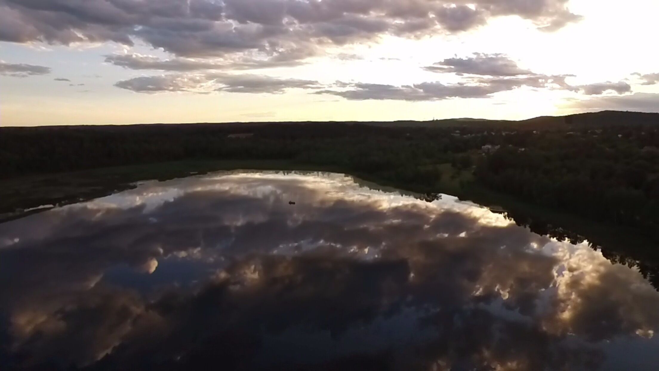 A body of water reflecting clouds and a hilly landscape.