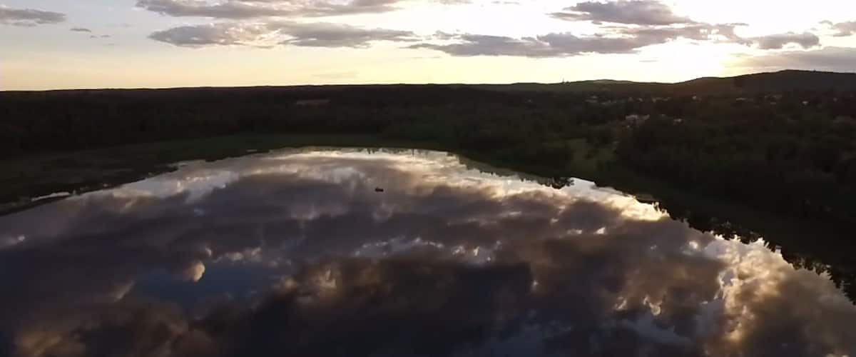 A body of water reflecting clouds and a hilly landscape.