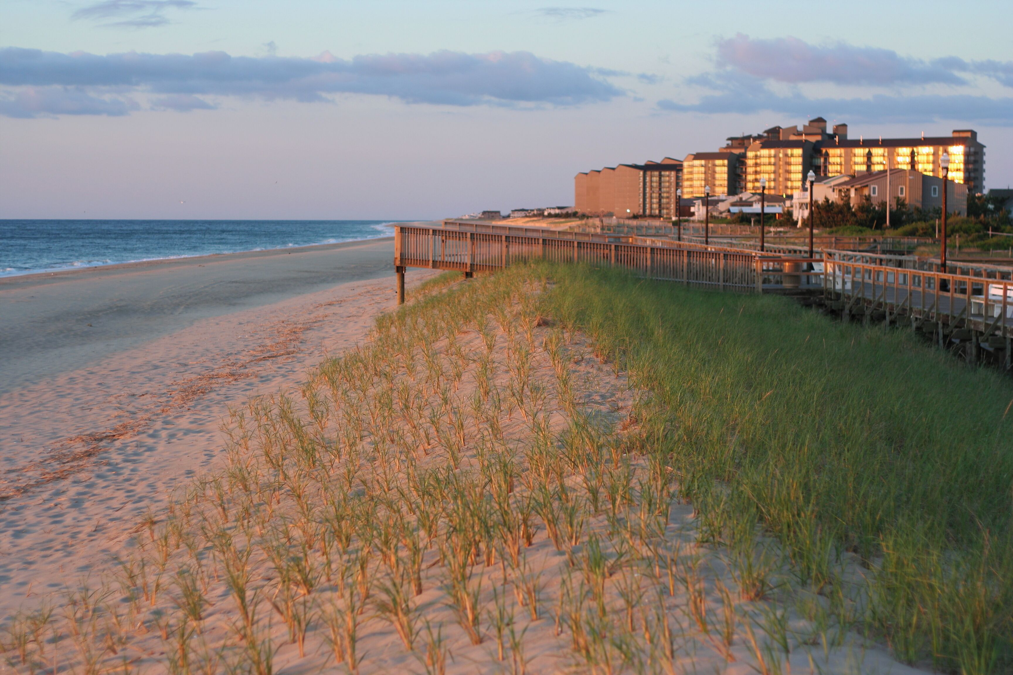 A beach with a wooden boardwalk leading to a hotel.