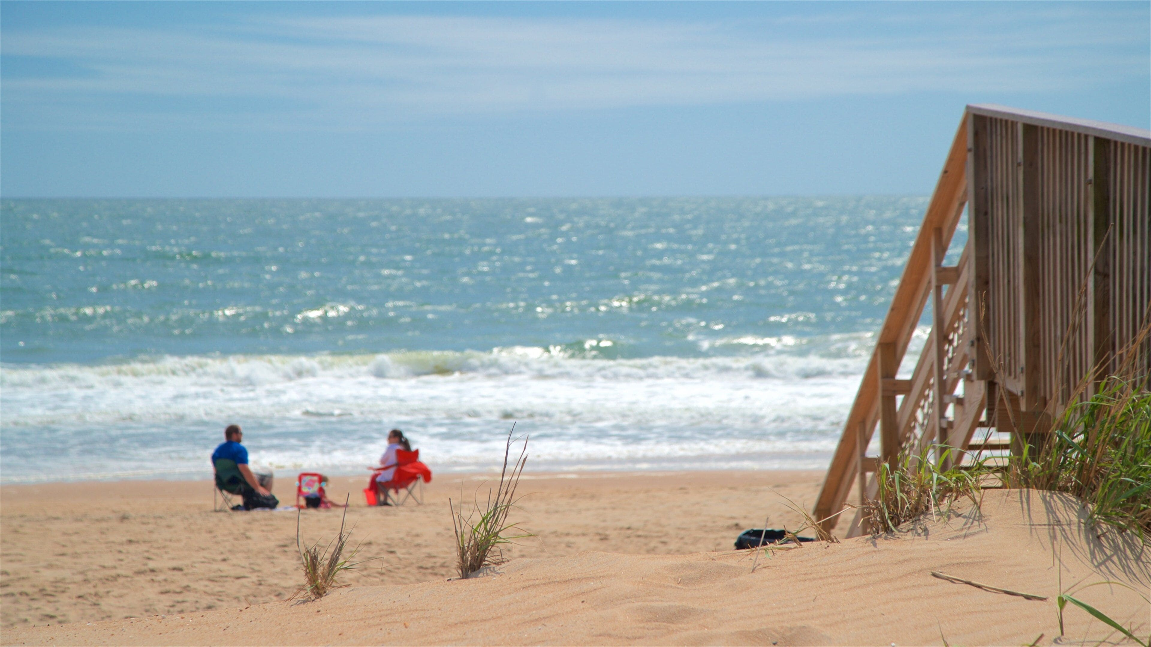 A beach with a wooden boardwalk, sand, and the ocean.