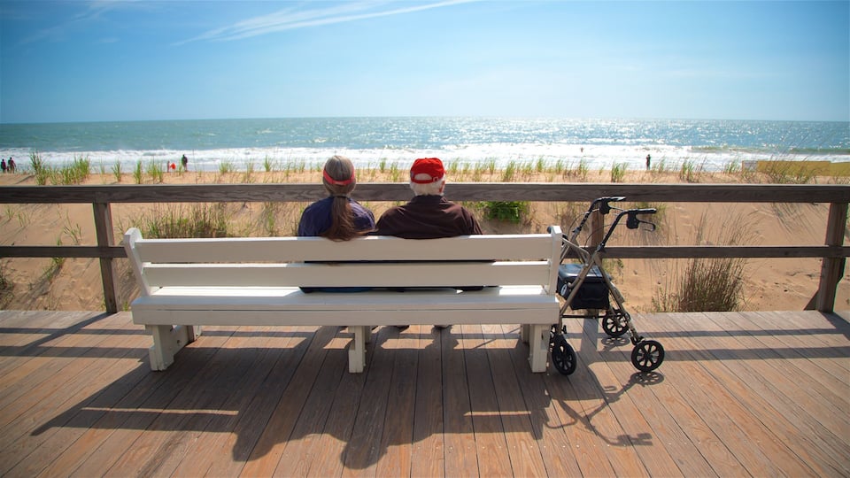 A wooden deck with a white bench overlooking a beach.