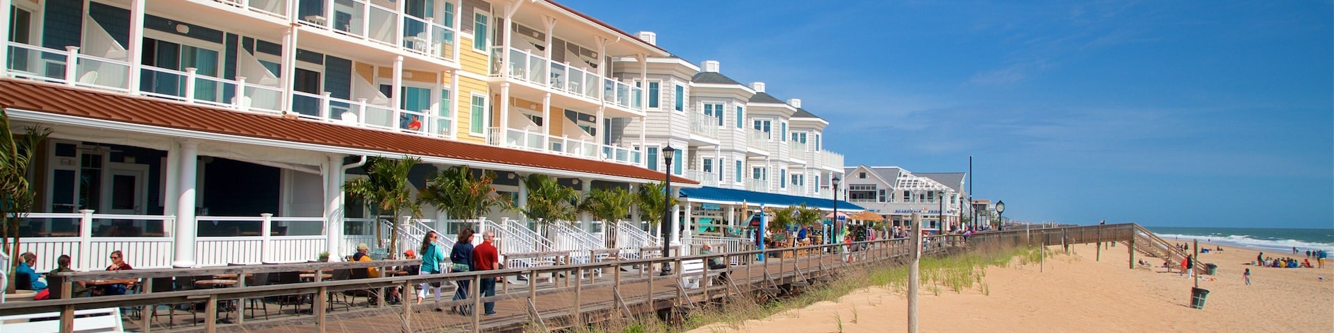 A beachside boardwalk with multi-story buildings, palm trees, and a sandy beach.