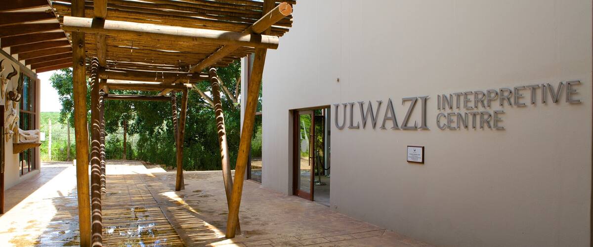 A covered walkway leading to the Ulwazi Interpretive Centre with a wooden pergola overhead.