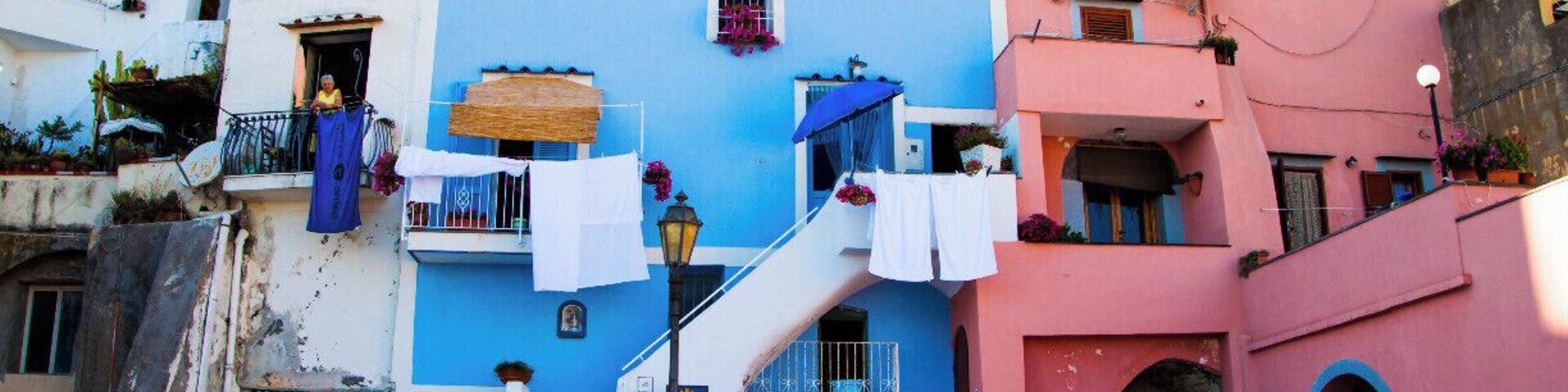Edificios coloridos con balcones y escaleras, una calle con peatones, y un cielo despejado.
